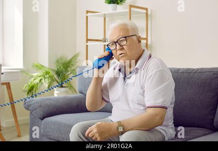 Retired senior man is talking on the telephone while sitting on the couch at home Stock Photo