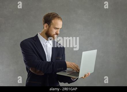 Studio portrait of serious concentrated adult caucasian businessman using laptop Stock Photo