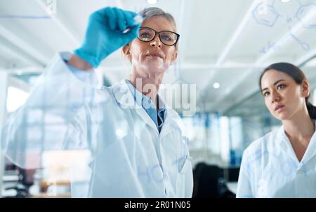 Planning and conducting some new experiments. two scientists drawing molecular structures on a glass wall in a lab. Stock Photo