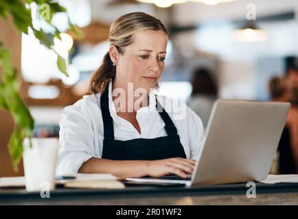 Taking charge of coffee shop management. a mature woman using a laptop and laptop while working in a cafe. Stock Photo