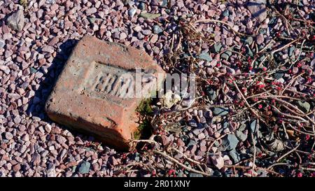 Pink colored stone pebbles to cover the ground with a fragment of brick. Brick fragment with vintage unidentified logo, overgrown with moss. Stock Photo