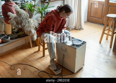 Concentrated craftswoman artist ceramist using potter wheel sits in studio to create clay sculpture Stock Photo