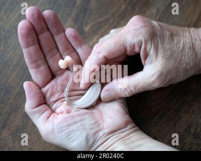 Using a hearing aid as a result of worsened hearing impairment. Hands hold hearing device, close up Stock Photo