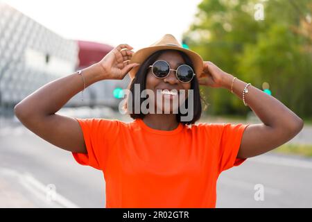 Summer vibes: Young black woman tourist in green t-shirt and sunglasses against brown wall, lifestyle photos Stock Photo