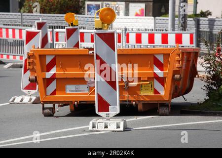 Container, orange skip for building rubble with barrier beacons standing on the road, construction site, road works, Germany Stock Photo