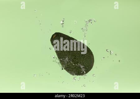 Fresh avocado on green background with water splash Stock Photo