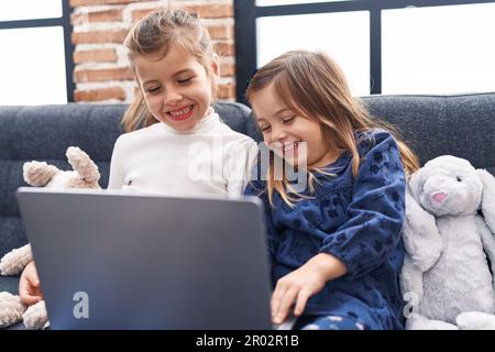 Adorable girls using laptop sitting on sofa at home Stock Photo