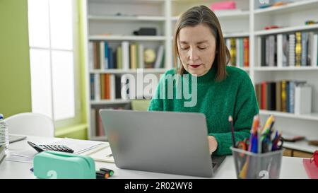 Mature hispanic woman with grey hair using laptop at library Stock Photo