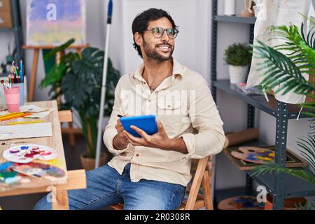Young hispanic man artist smiling confident using touchpad at art studio Stock Photo