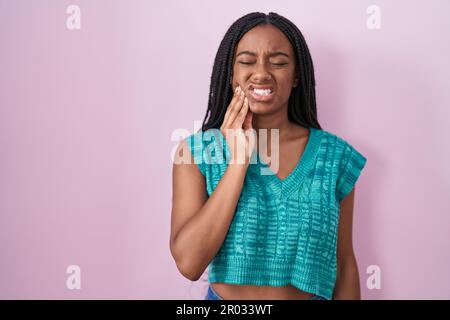 Young african american with braids standing over pink background touching mouth with hand with painful expression because of toothache or dental illne Stock Photo
