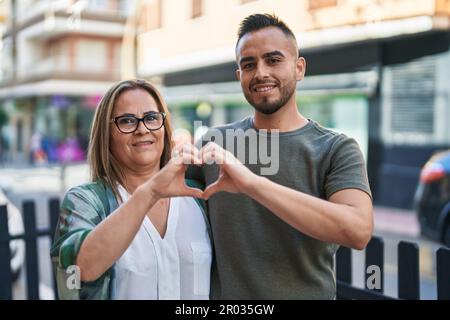 Man and woman mother and daugther doing heart gesture with hands at street Stock Photo