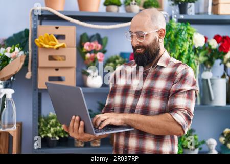 Young bald man florist smiling confident using laptop at flower shop Stock Photo