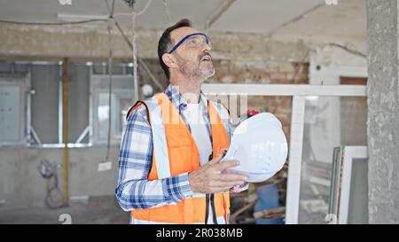 Middle age man builder tired using hardhat as a hand fan at construction site Stock Photo