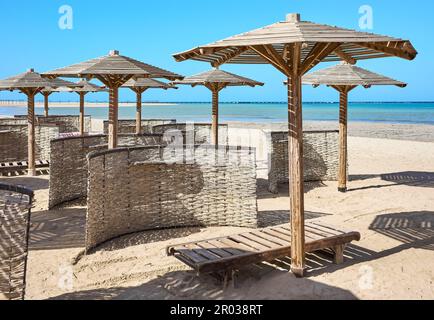 Wooden sun umbrellas, sun beds and windscreens on beach. Stock Photo