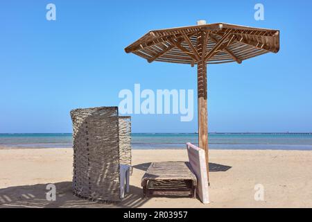 Wooden sun umbrella, sunbed and windscreen on beach. Stock Photo