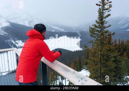 A traveler man standing and enjoying the view of Peyto lake similar a fox with snowfall in winter at Banff national park, AB, Canada Stock Photo
