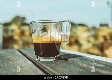 A glass of espresso sits on a table in front of a blurred background. Stock Photo