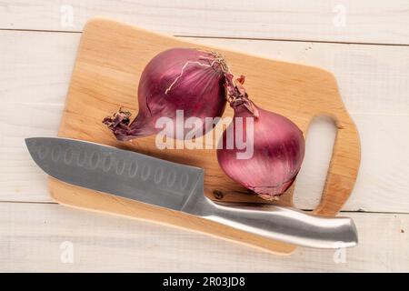 Two organic blue onions with knife and wooden kitchen board on wooden table, macro, top view. Stock Photo