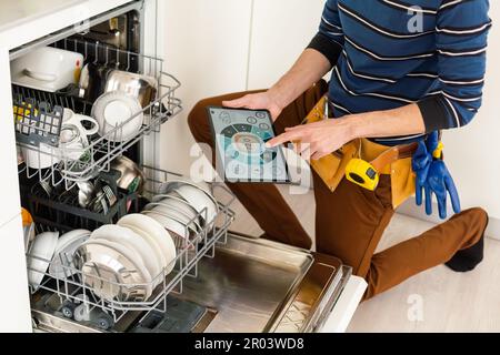 Portrait Of Male Technician Repairing Dishwasher In Kitchen using digital tablet. Stock Photo