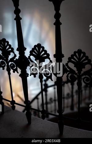 Decorative wrought iron banister detail. Selective focus. Spiral staircase. Colored window glass reflection in the background. Stock Photo