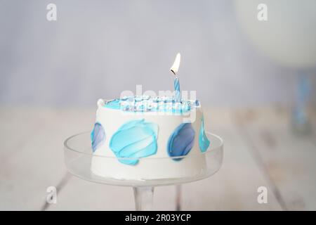 white and blue cake with one candle. small lunch box blue cake with one blue candle on a white background. boys birthday cake on a glass plate with ca Stock Photo