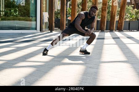 Fit sporty young black man doing warm up exercises in workout park. Stock Photo