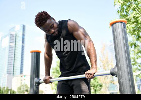 Fit sporty young black man doing dip bar exercises in workout park. Stock Photo