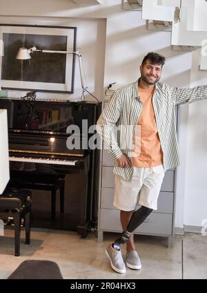 Happy young man with above knee leg prosthesis standing at home. Stock Photo