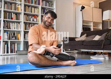 Happy man with prosthetic leg disability doing yoga using phone at home. Stock Photo
