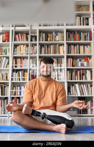 Amputee man with prosthetic leg prosthesis meditating doing yoga at home. Stock Photo