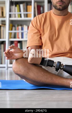 Amputee man with prosthetic leg prosthesis meditating doing yoga at home. Stock Photo