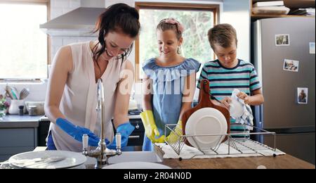 Theyre learning from the best. an affectionate young mother doing the dishes with her two children in their kitchen at home. Stock Photo
