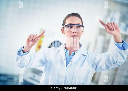 Using both fingers. a focused young female scientist wearing protective glasses while pointing with her finger on a glass wall. Stock Photo