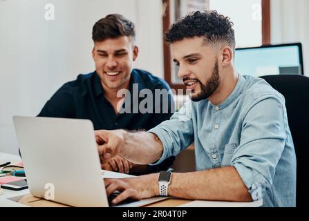 Twice the creative talent. two young businessmen using a laptop together in a modern office. Stock Photo