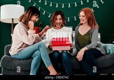 I think she might like the gift. three attractive middle aged women opening presents together while being seated on a sofa during Christmas time. Stock Photo