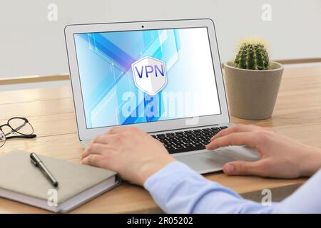 Man using laptop with switched on VPN at wooden table indoors, closeup Stock Photo