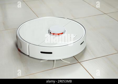 Robotic vacuum cleaner on white tiled floor Stock Photo