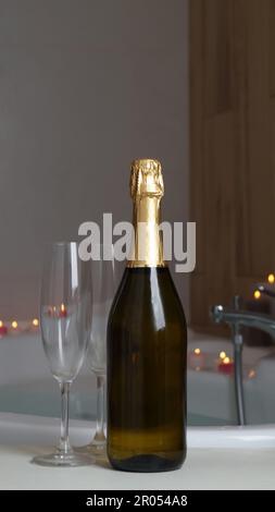 Sparkling wine, glasses and burning candles near jacuzzi in bathroom Stock Photo