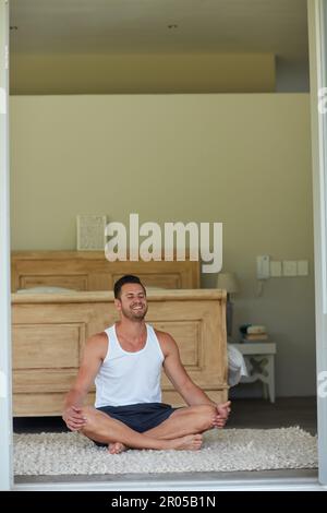 Meditation makes him calm in the mornings. a young handsome man practicing yoga at home. Stock Photo