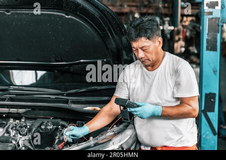 Experienced auto mechanics inspect car battery terminals and voltage to