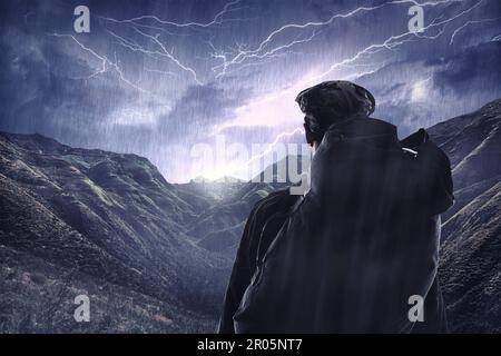 Lightning storm, travel and a man hiking from the back in the mountains during the night with winter rain. Dark sky, gray clouds and stormy weather Stock Photo