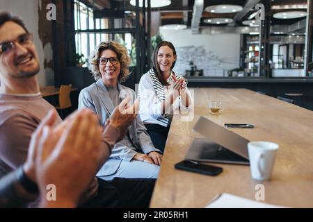 Colleagues applauding during a team meeting in an office. Group of business people celebrating success in a boardroom. Happy professionals working tog Stock Photo