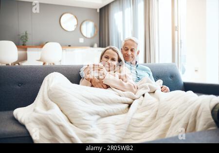 Under the blankets where its warm and cosy. a mature couple relaxing on the sofa at home. Stock Photo