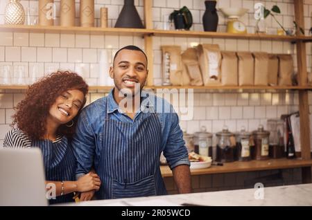 A couple that owns businesses together stay together. an affectionate young couple standing together behind the counter in their cafe. Stock Photo