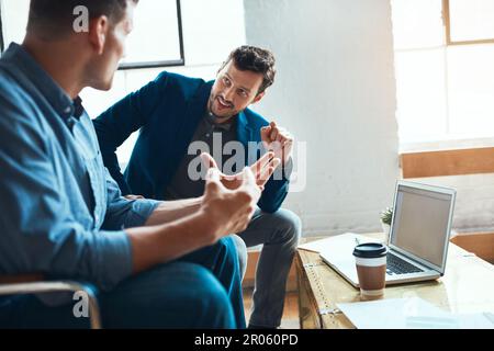 Collaborating on creative content. two young businessmen having a discussion and using a laptop together in a modern office. Stock Photo