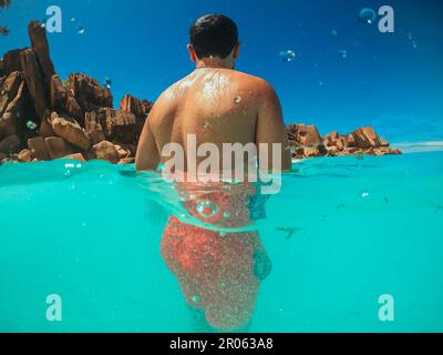 A man in red swimming trunks stands in the sea against a tropical beach Stock Photo