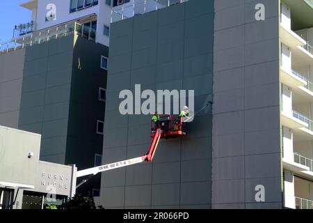 Two people painting an apartment building wall using a crane Stock Photo