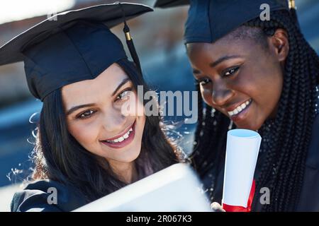 Snapping memories of their biggest milestone. two students taking a selfie together on graduation day. Stock Photo