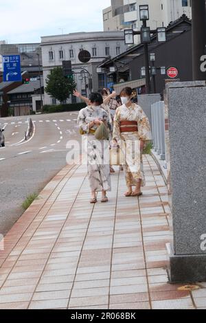 A group of young girls wearing masks and summer kimonos called yukata while walking across a bridge in the summer heat and talking Stock Photo