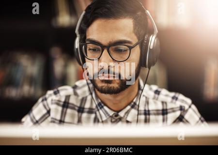 Theres no distracting his focused mindset. a university student working on a computer in the library on campus. Stock Photo